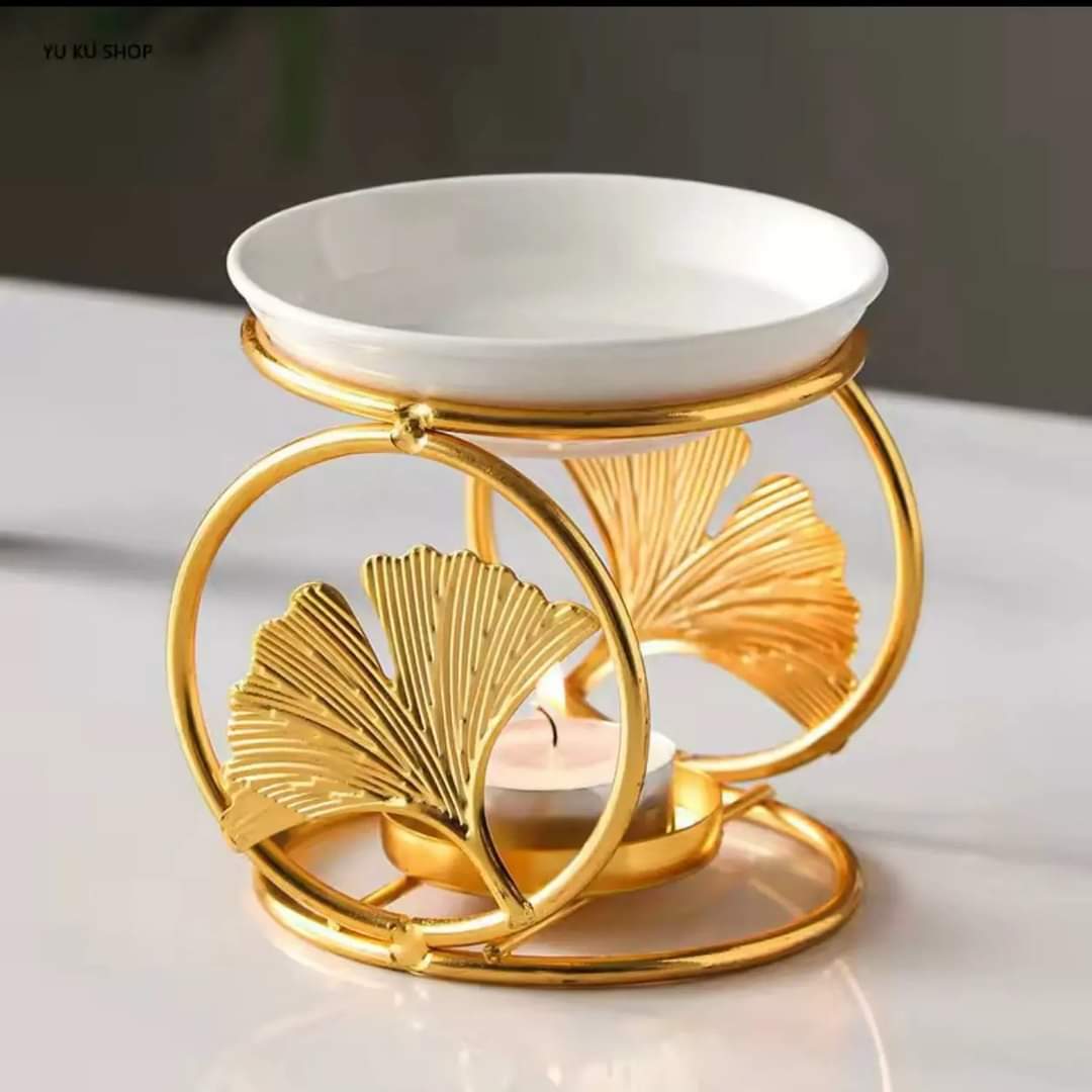 A decorative gold metal oil burner with ginkgo leaf details and a white ceramic bowl.
