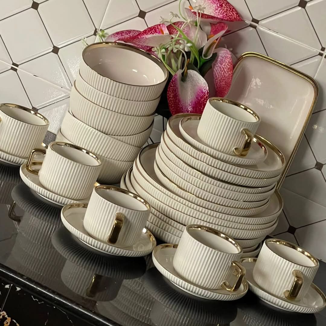 A 32-piece dinner set displayed, including cups, saucers, side plates, bowls, plates, and two platters, predominantly white with gold accents.