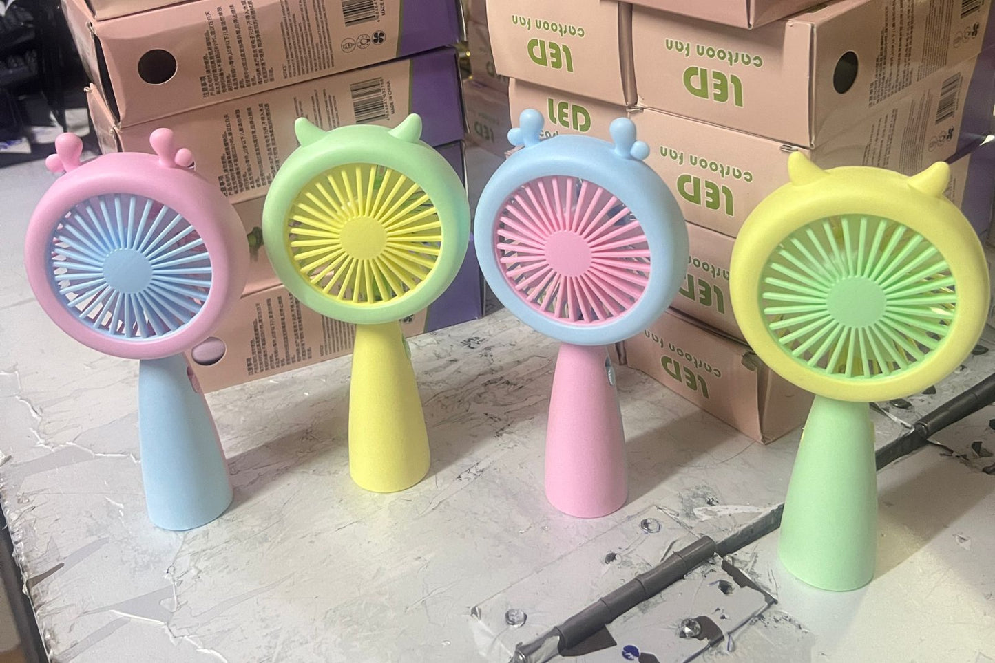 A collection of colorful, cartoon-themed handheld mini-fans in pastel shades of pink, purple, blue, yellow, and green.