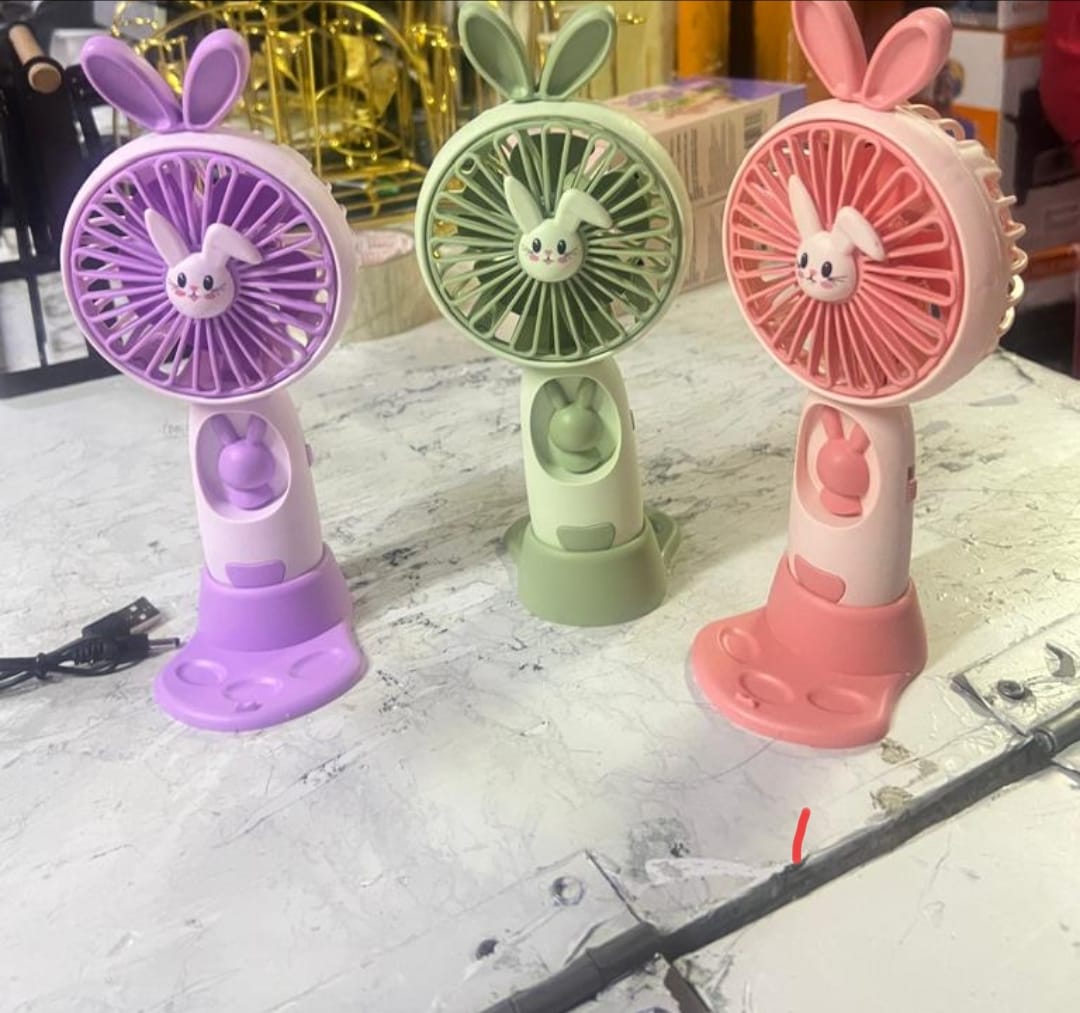 Three bunny-eared mini fans in purple, green, and pink colors, sitting upright on a table with a USB cable visible.