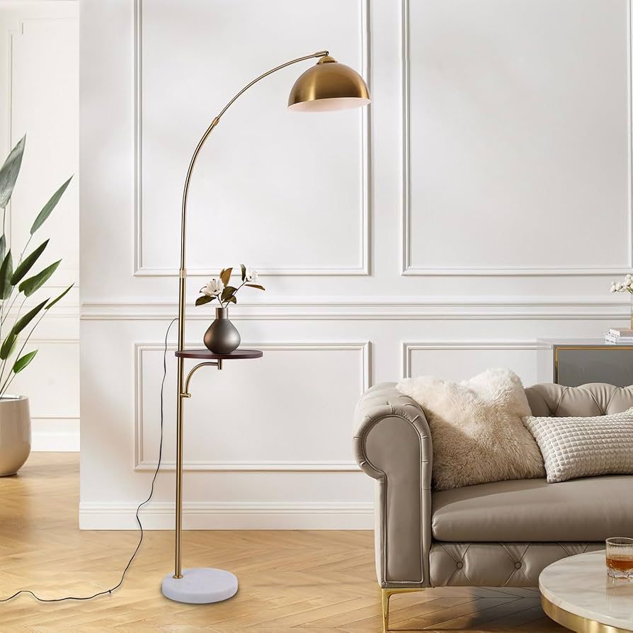 An arc floor lamp with a brass metal frame, a brass dome shade, a small built in wooden table shelf, and a white marble base.
