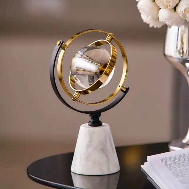 A clear crystal ball suspended in gold metallic rings on a white marble base.