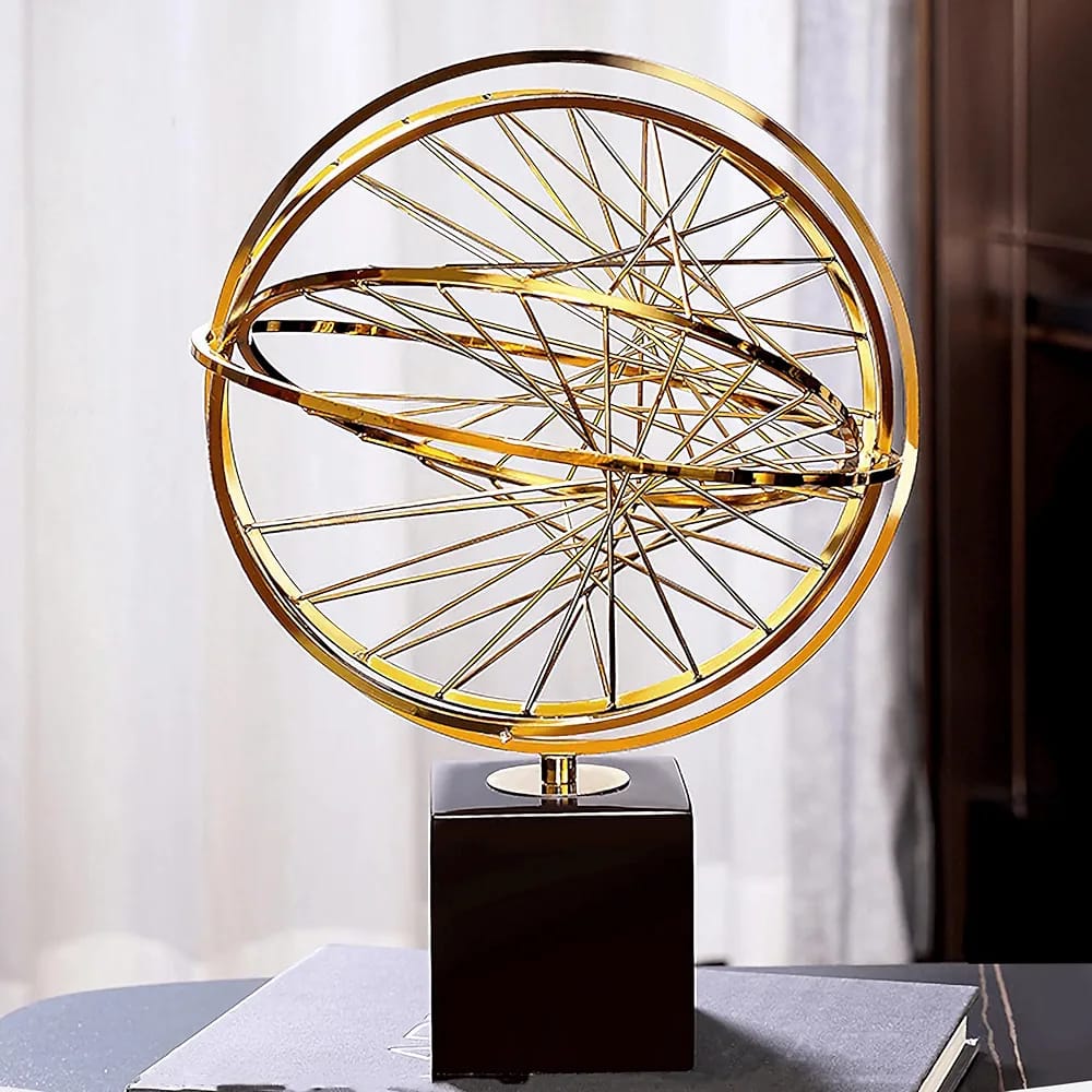 A gold metallic globe sculpture with intersecting spokes on a black square base.