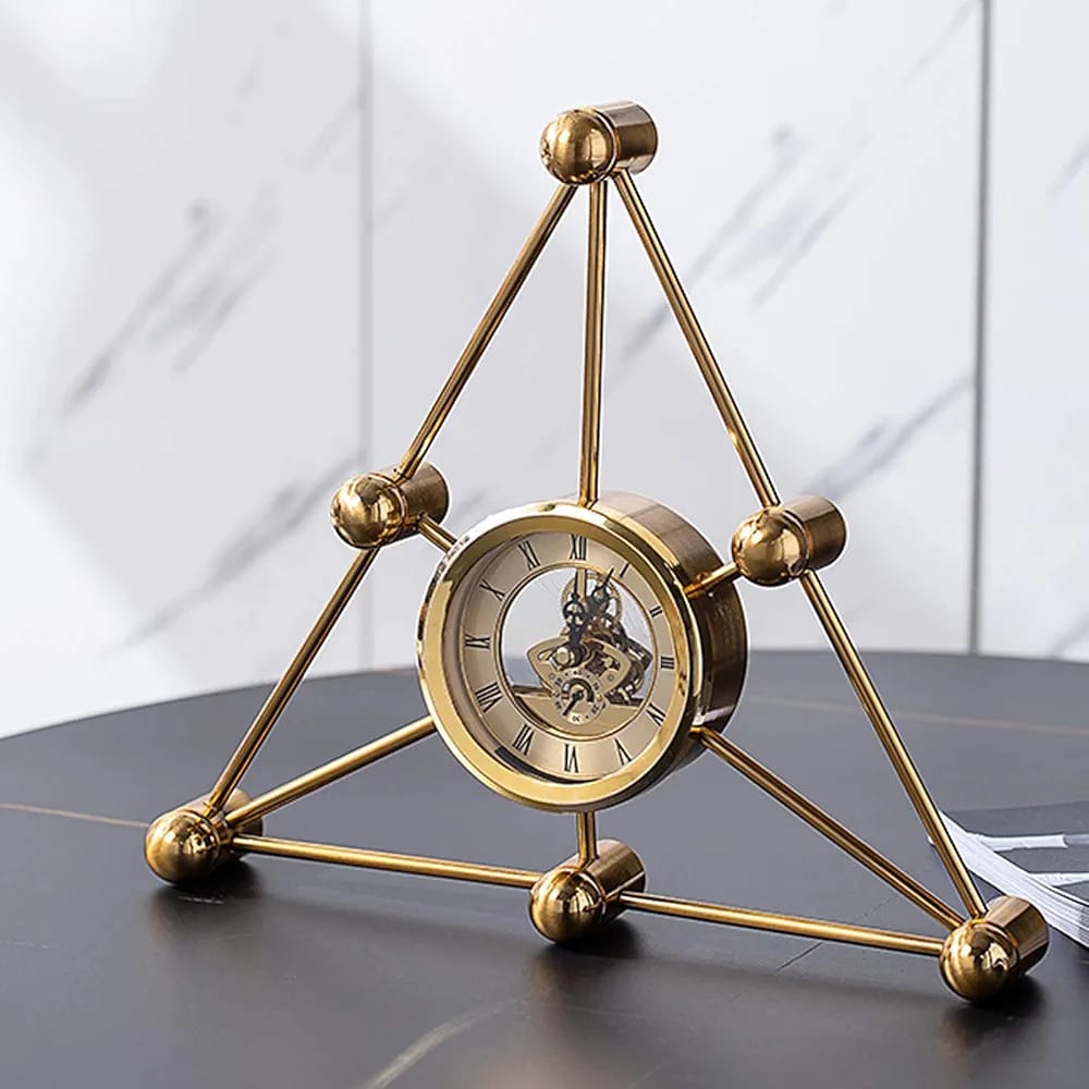 A gold-colored metal desk clock in a triangular shape with a roman numeral clock face.