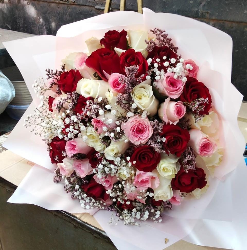 A large, lush, hand-tied bouquet featuring twenty fresh roses in mixed colors like red, pink, and white, accented with delicate white filler flowers, wrapped in pale paper.