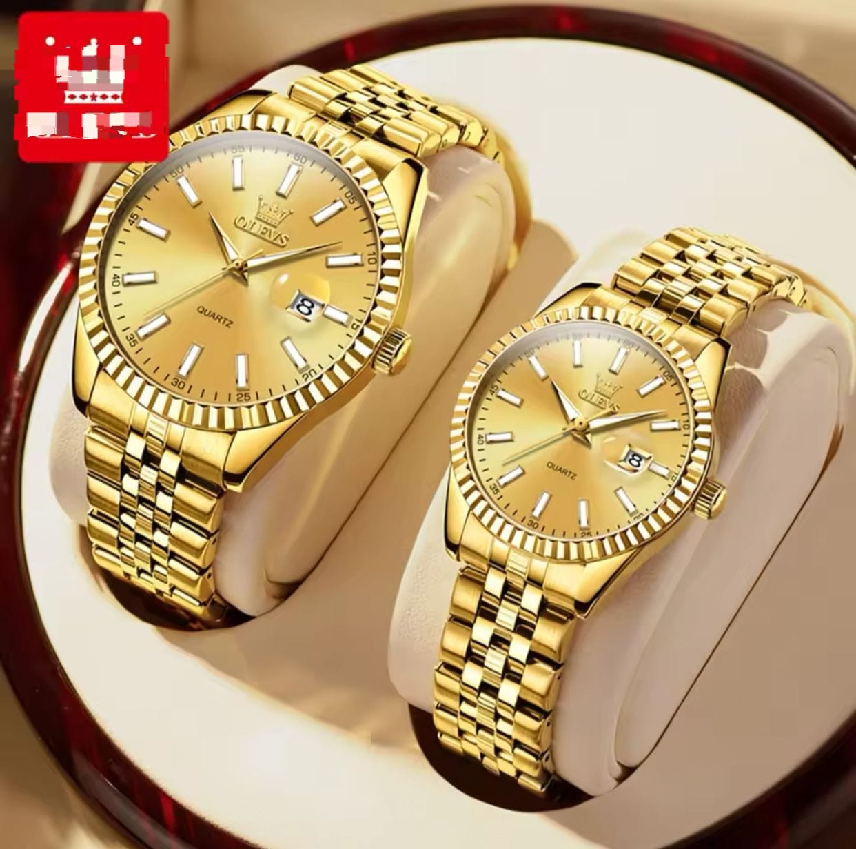 A pair of gold toned, stainless steel Olevs couple watches with metal link bands and date displays, sitting side by side on light colored watch pillows.