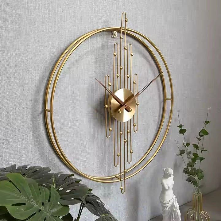 large gold metal wall clock with a double ring frame and vertical rod accents.