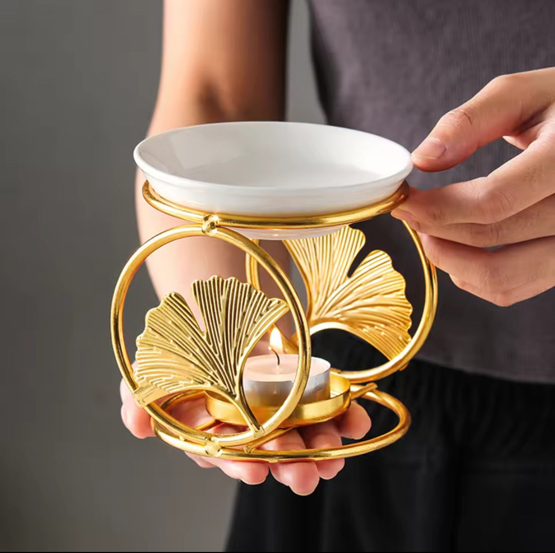 A gold metallic ginkgo leaf frame holding a white ceramic bowl and a lit tea light candle.