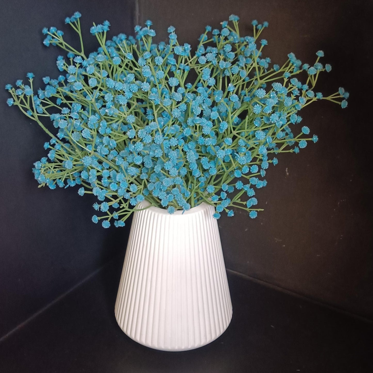 A cluster of blue artificial baby's breath flowers in a white ribbed plastic vase
