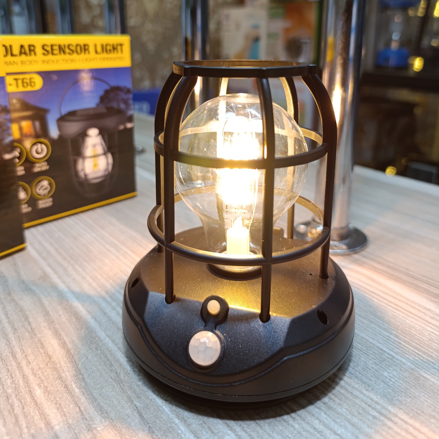 A black solar lantern with a warm glowing LED bulb protected by a cage frame.
