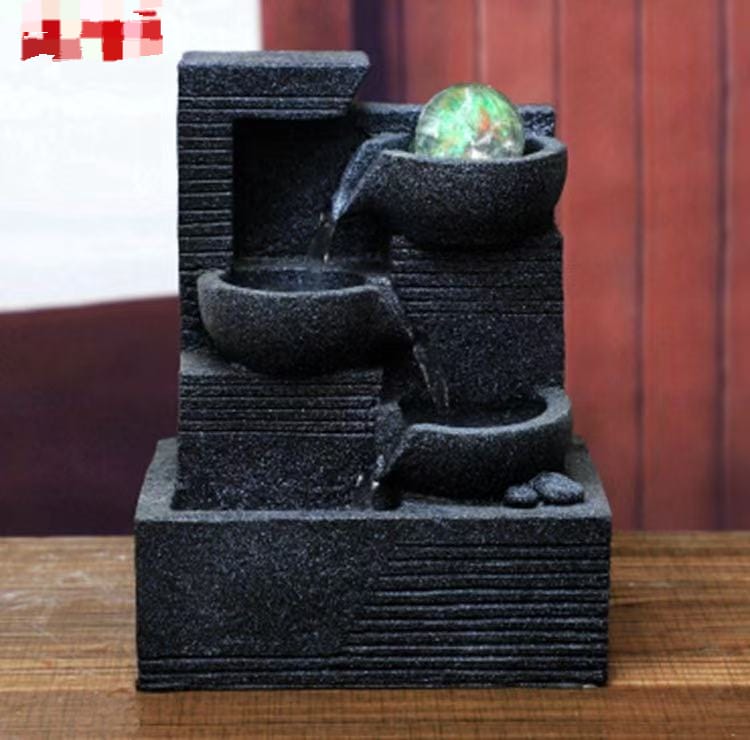 A three-tier stone-textured tabletop fountain with a glowing glass ball and flowing water.