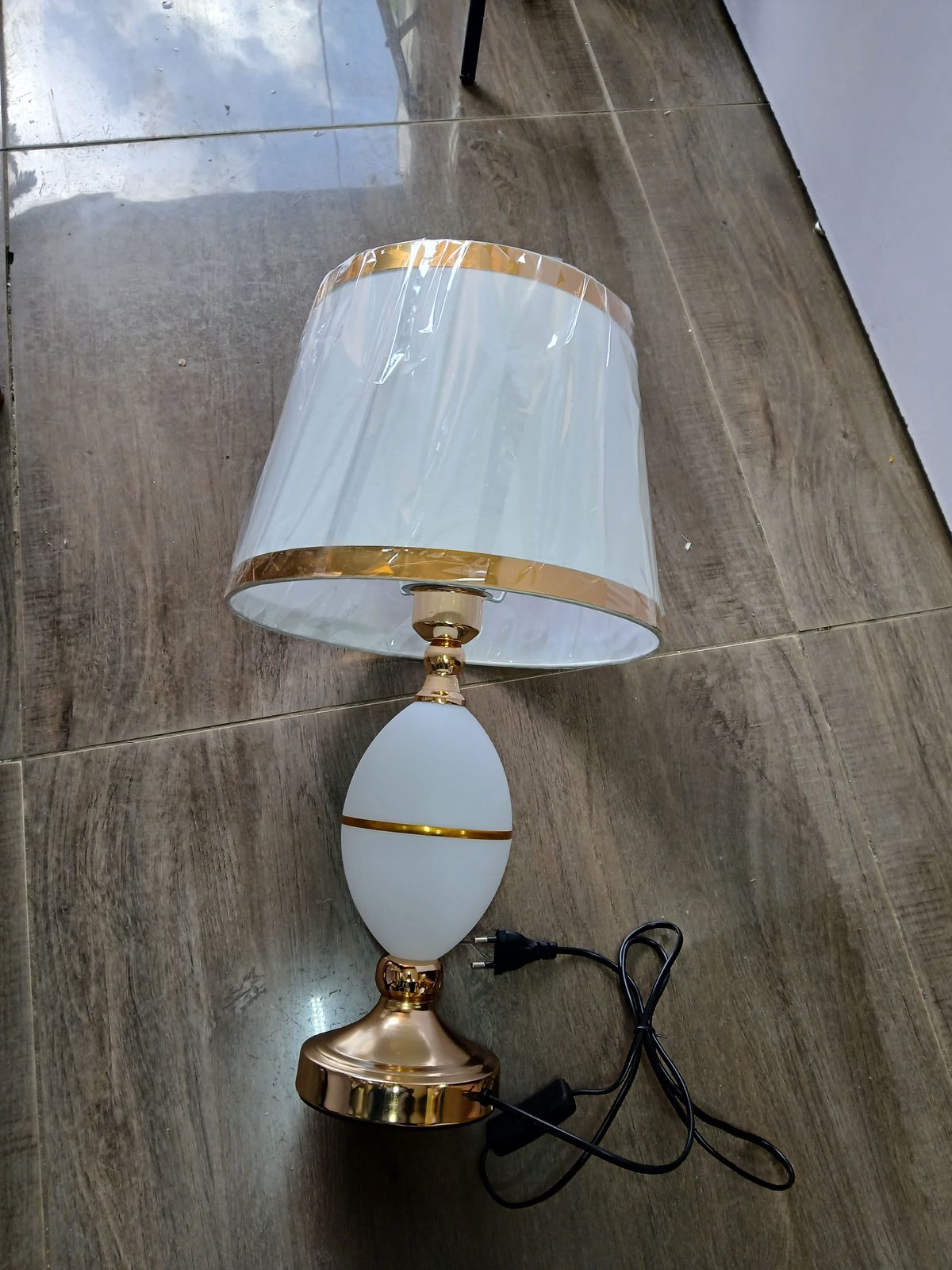 A white and gold bedside lamp with an oval base and gold-trimmed lampshade