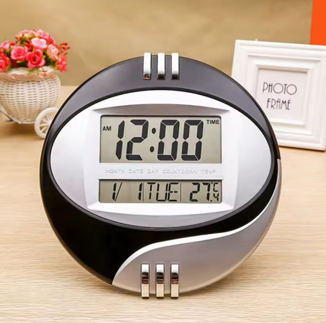 Oval black and silver digital clock with a liquid crystal display.