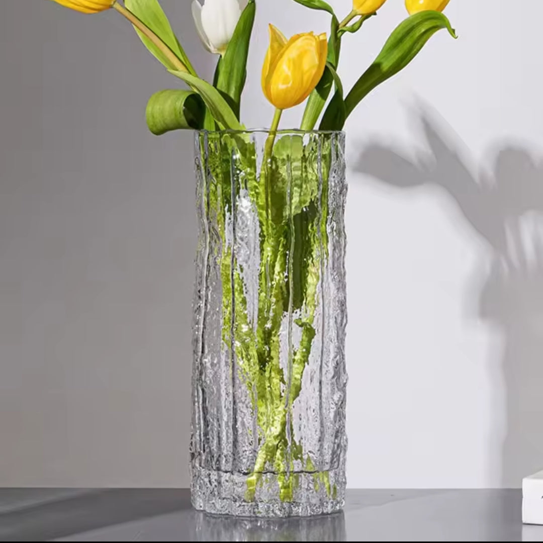 A metallic gold vase with a wavy embossed texture holding green leafy stems.