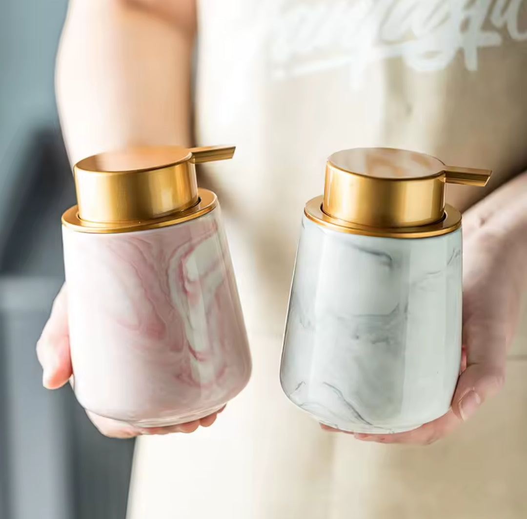 Two marble-patterned soap dispensers with gold pumps held by a person.