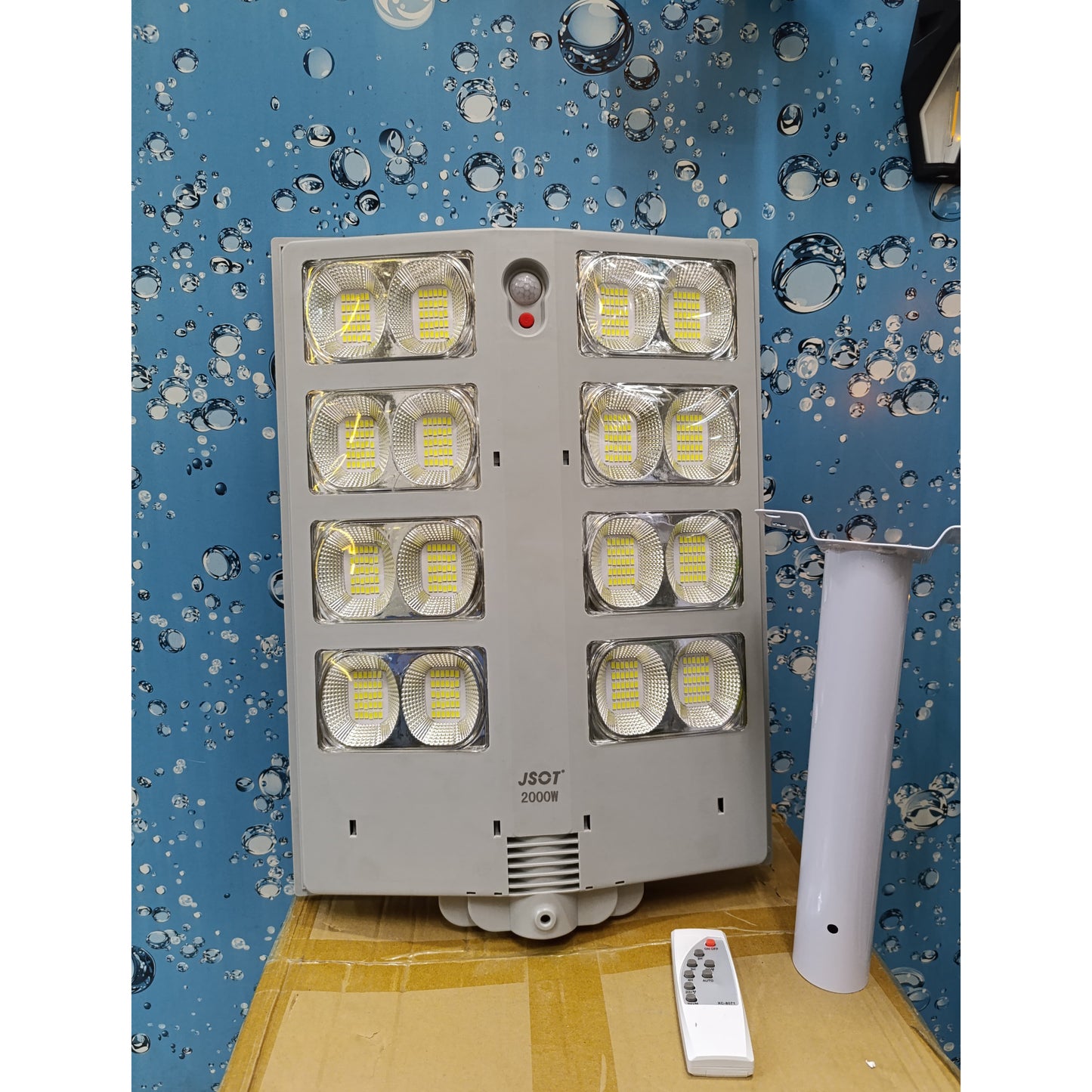 A large grey JSOT 2000W solar street light with eight LED panels, a mounting pole, and a remote control.