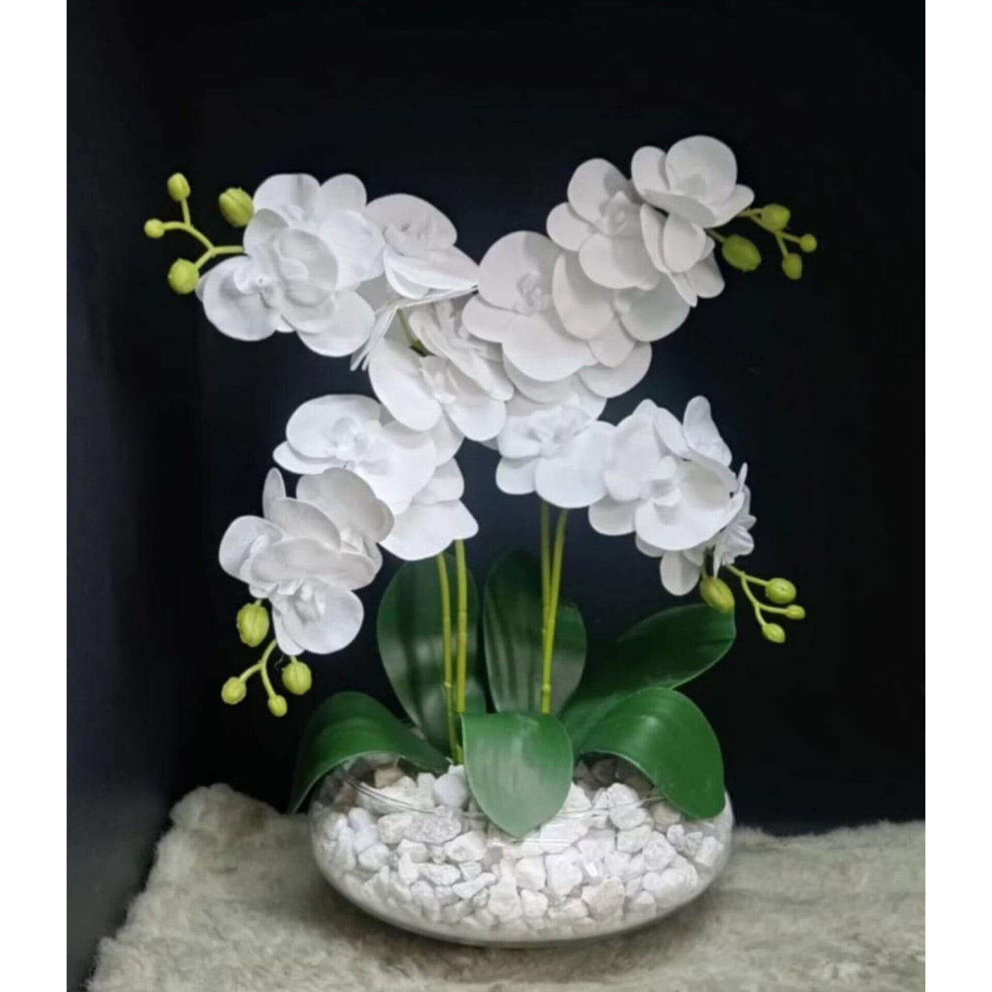A clear glass vase containing tall artificial orchid flowers with visible green stems.