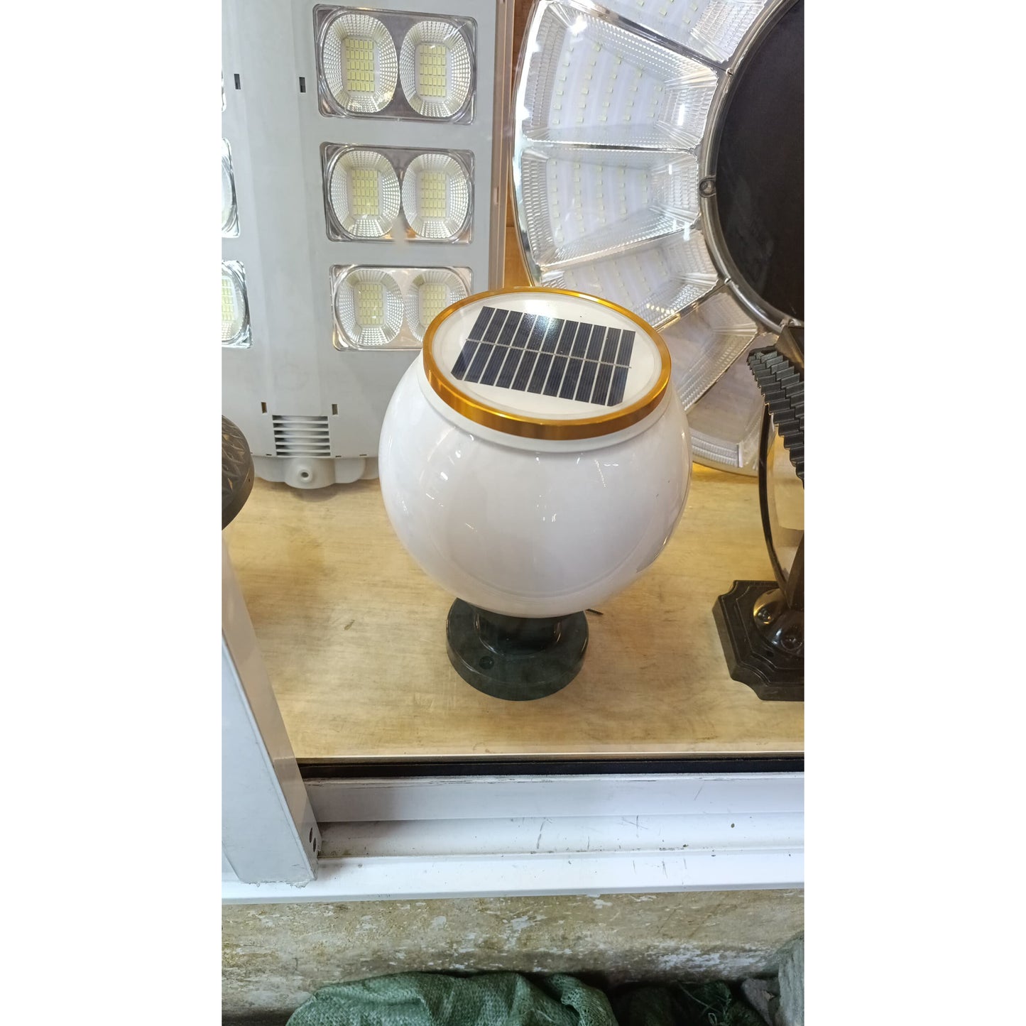 A white spherical solar garden light with a gold rimmed solar panel on top and a dark mounting base.