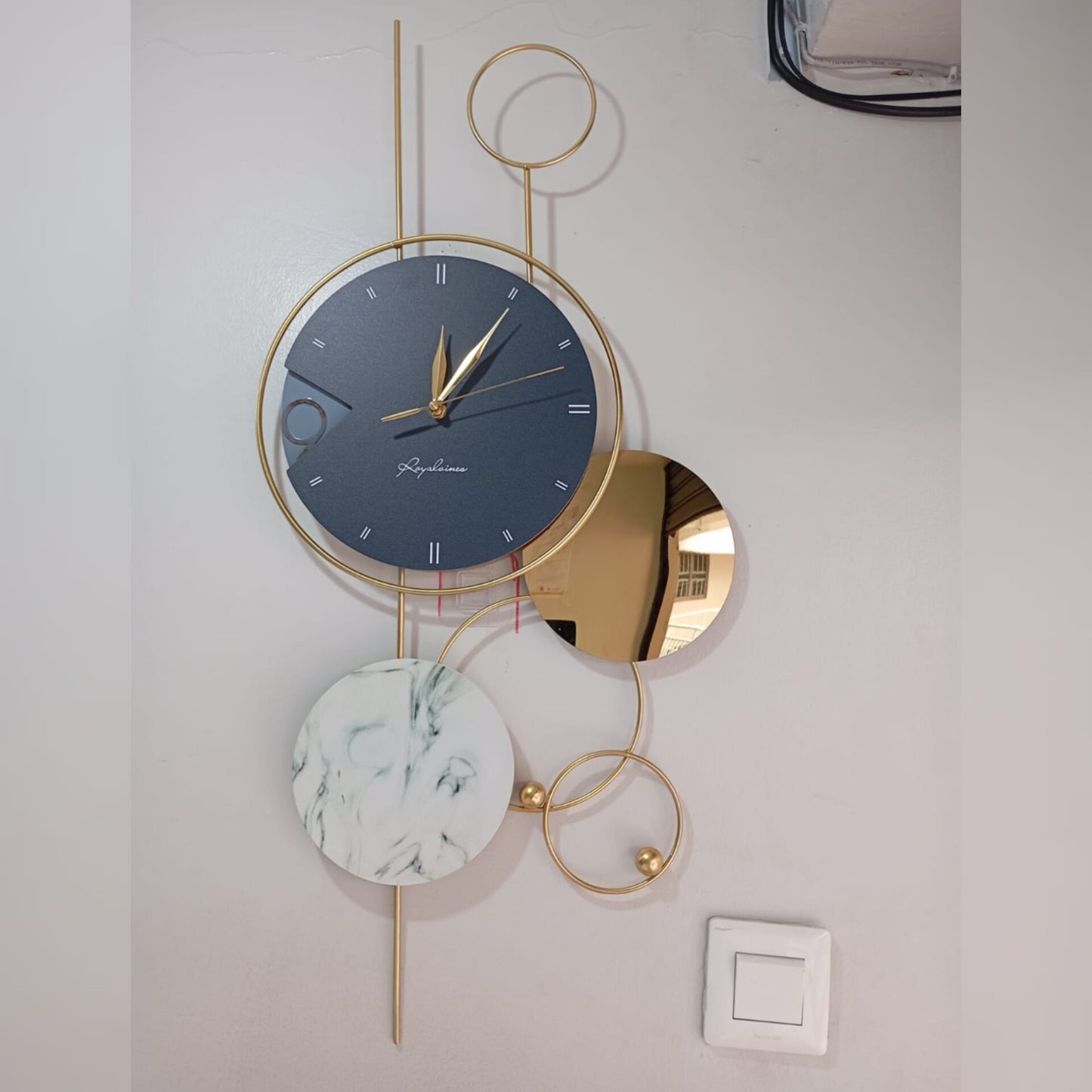 A large, modern, vertical wall clock made of gold-colored iron art, featuring a dark blue dial, a small round mirror, and a white marble patterned circle.