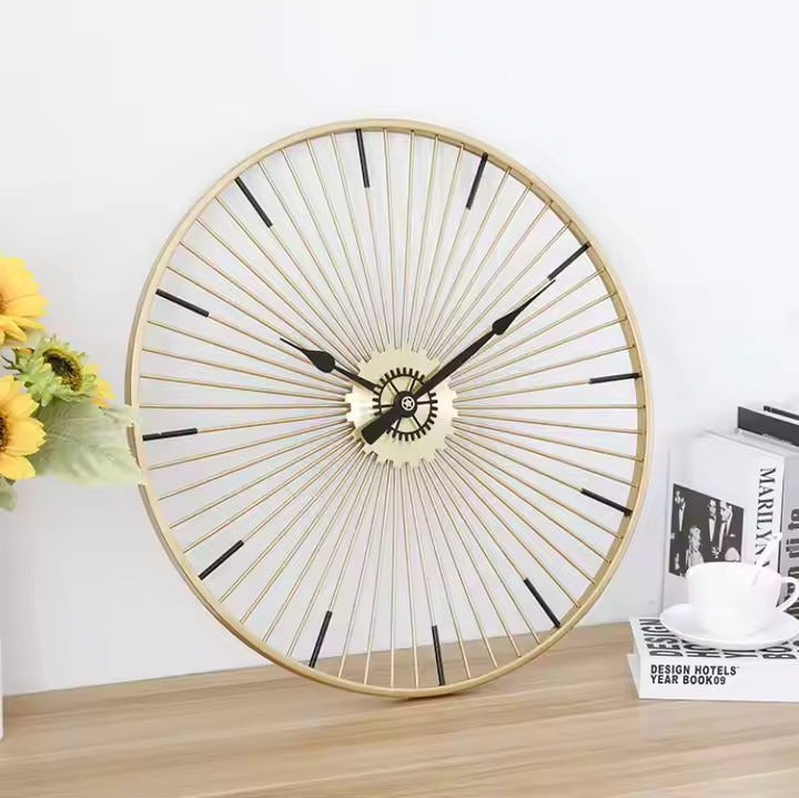 A gold metal wall clock designed like a bicycle wheel with black hands.