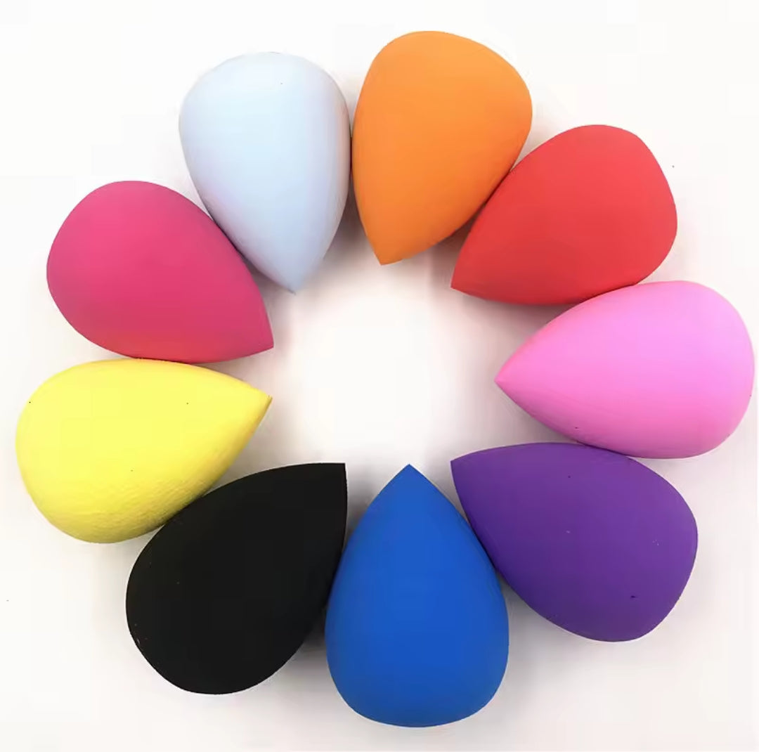 A circular arrangement of nine colorful tear-drop shaped makeup sponges in shades including pink, orange, yellow, black, blue, and purple on a white background.