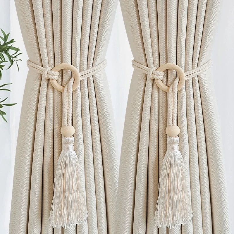 A pair of cream woven cotton curtain tiebacks with wooden rings and long tassels.