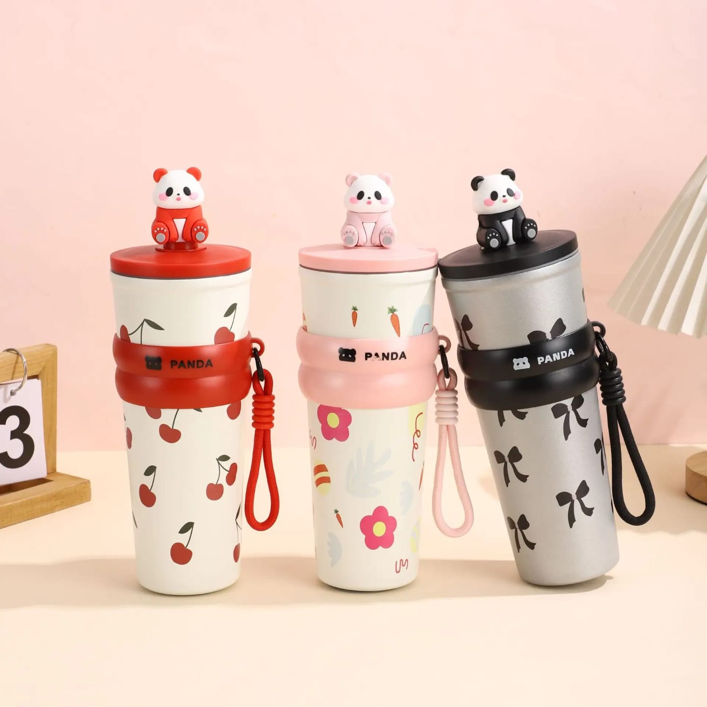 A white and pink 700 milliliter insulated Stanley cup with a panda pattern, a handle, a straw, and a small 3D panda figure on top of the lid.