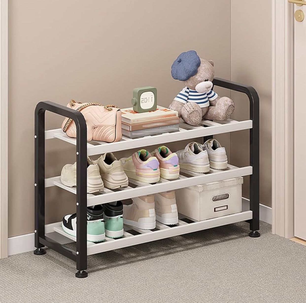 Three-tiered shoe rack with white shelves and black metallic frame, holding various pairs of shoes, a handbag, a clock, and a teddy bear.