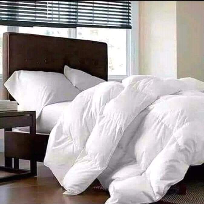 A fully made bed featuring a white fluffy duvet, white pillows, and a white bed sheet.