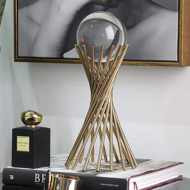 A transparent glass sphere resting on a gold metal stand made of rods arranged in an hourglass shape.