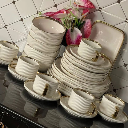 A 32-piece dinner set displayed, including cups, saucers, side plates, bowls, plates, and two platters, predominantly white with gold accents.