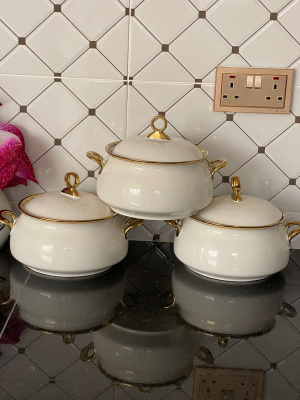 Three white ceramic serving bowls with gold rims and handles