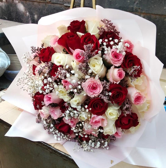 A large, lush, hand-tied bouquet featuring twenty fresh roses in mixed colors like red, pink, and white, accented with delicate white filler flowers, wrapped in pale paper.