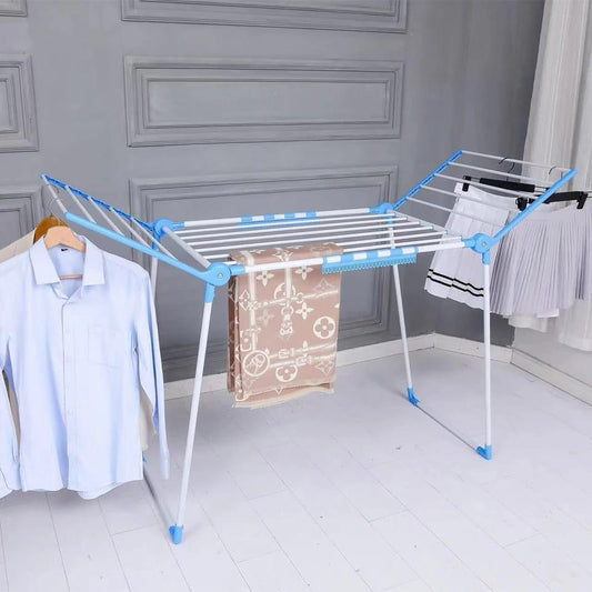 A large, white and blue foldable clothes drying rack with two adjustable wings, holding a blanket and shirts in a modern room.