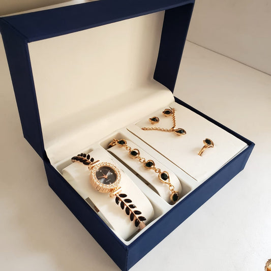 A dark blue gift box open to show a gold-toned ladies' watch with a black strap, a matching bracelet with black stones, black earrings, a necklace, and a ring.