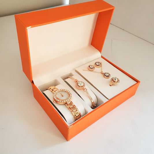 An orange gift box open to show a rose gold-toned ladies watch with crystals, a matching bracelet, necklace, earrings, and ring.