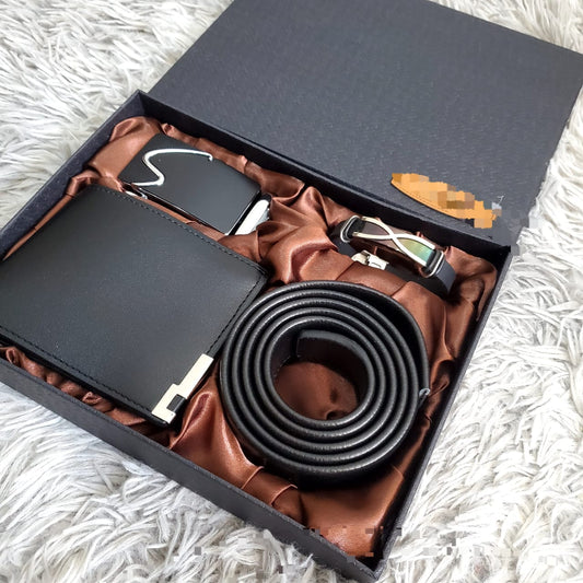 Black men's gift set in an open black box with brown satin lining, containing a coiled black belt, a black bifold wallet, and a silver belt buckle.