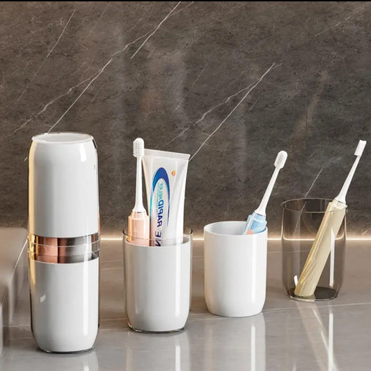 A white and rose gold portable travel toothbrush holder and case, displayed on a counter alongside two separate matching rinsing cups holding toothbrushes and toothpaste.