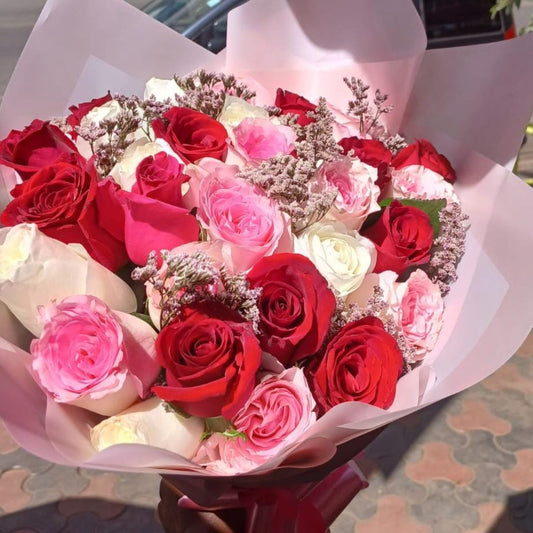 A hand holding a large, beautiful bouquet of fresh roses in mixed colors including deep red, bright pink, and white, wrapped in light pink paper.