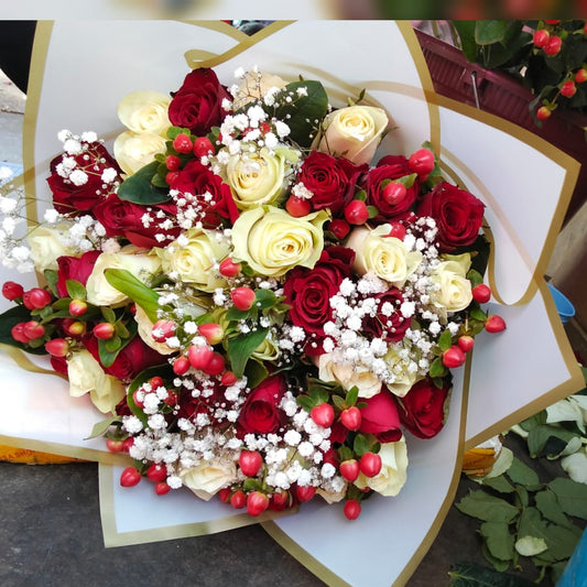 A lush, romantic bouquet of fresh red and creamy white roses, accented with small red berries and white baby's breath filler, wrapped in white and gold paper.