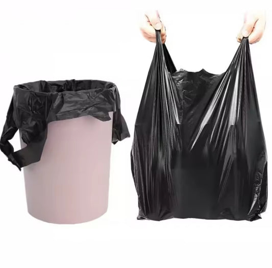 A black trash bag lining a light pink trash can on the left, and a person holding up a single open black trash bag by its integrated handles on the right.