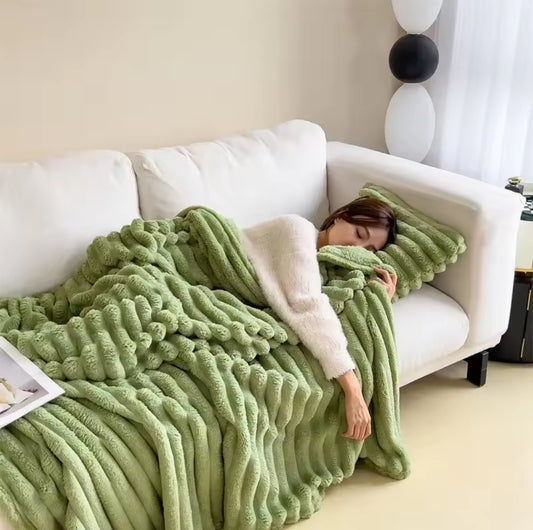 A thick, soft, green throw blanket with a large ridged bubble texture draped over a white couch, with a person sleeping comfortably underneath it.
