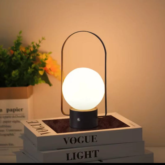 A modern table lamp with a glowing white spherical shade, a black cylindrical base, and a thin black arched metal frame.