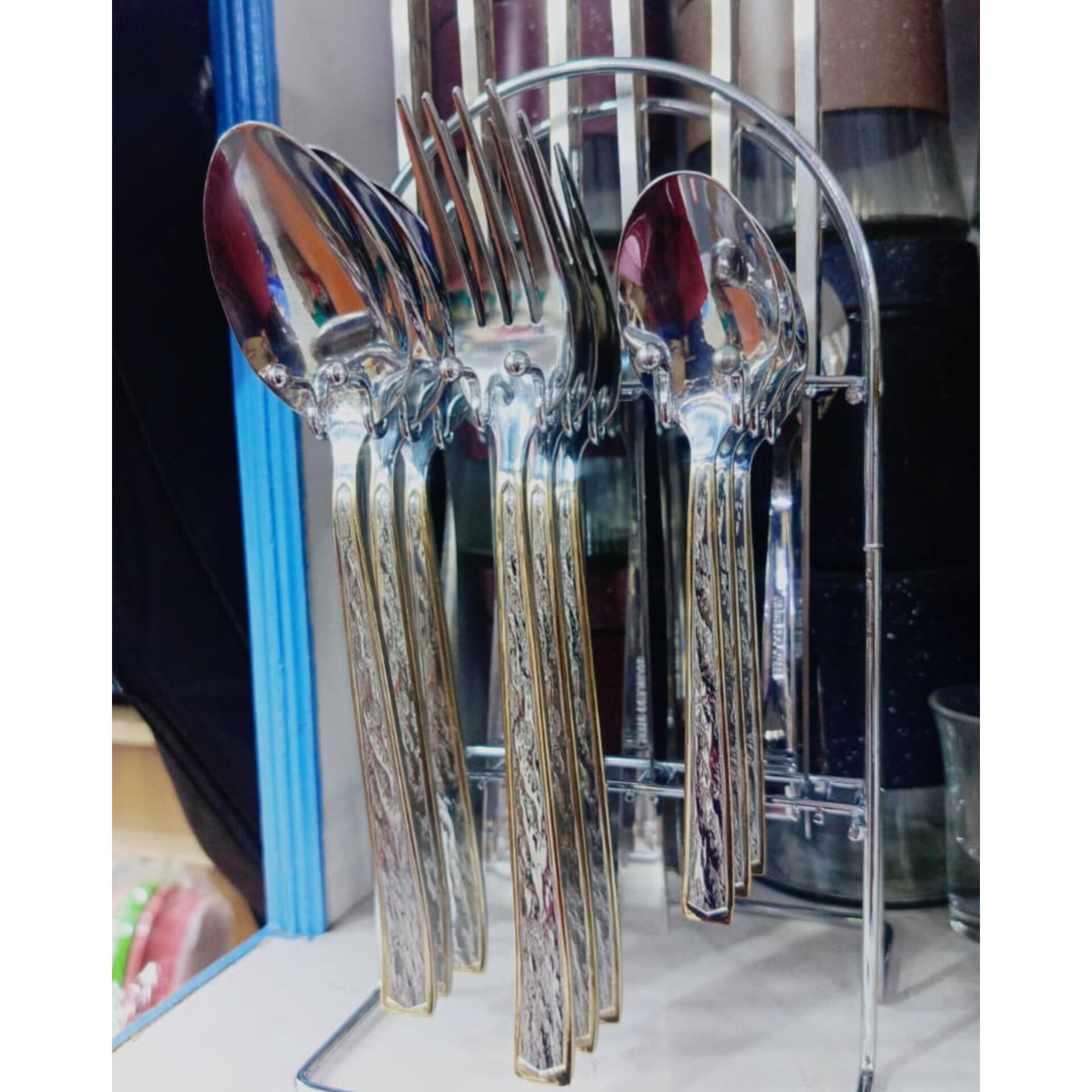Shiny 24-piece stainless steel cutlery set with gold-textured handles and a metal storage stand.