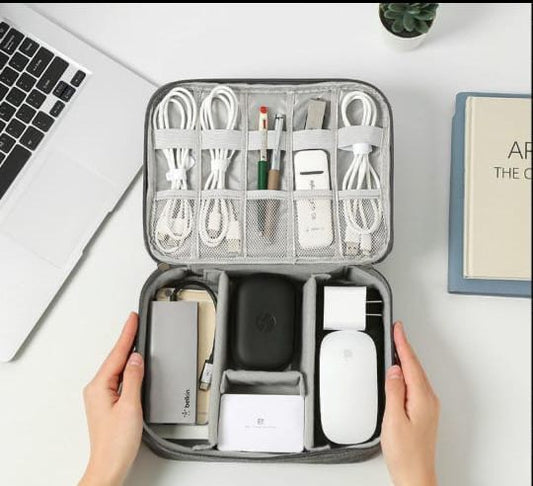 An open gray zippered organizer bag showing two layers of storage: the top layer has elastic loops holding coiled white cables, and the bottom layer holds a power bank, charger, and mouse.