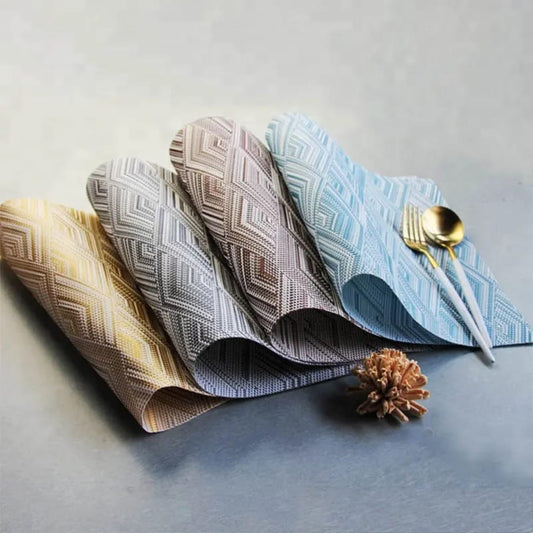 Four rolled PVC place mats in different colors (gold, grey, brown, and blue) with a geometric woven pattern.