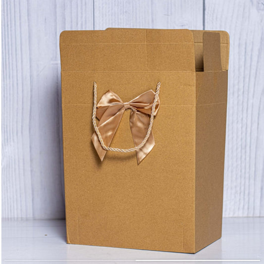 A tall, portrait oriented brown Kraft cardboard gift box with gold rope handles and a large decorative gold silk bow.