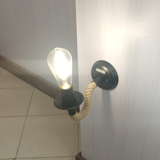 A black wall mounted light fixture with a thick braided rope arm holding a lit clear glass bulb.