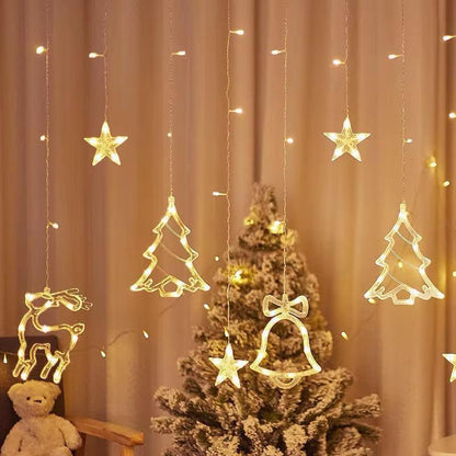 Decorative string lights shaped like stars, trees, and a bell hanging above a Christmas tree.