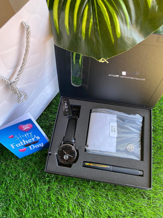 A black Father's Day gift set containing a black watch, a black leather wallet, and a black pen in a presentation box, next to a Father's Day card and a white gift bag.